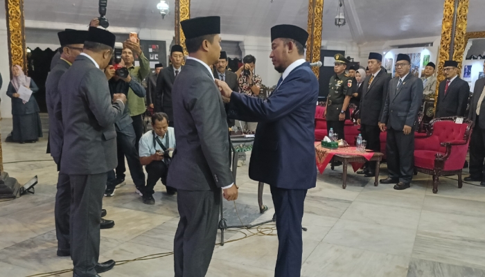 DIKUKUHKAN. Bupati Sumenep Achmad Fauzi Wongsojudo menyematkan tanda jabatan kepada Kamarullah saat pelantikan Komisioner Komisi Informasi Kabupaten Sumenep periode 2025–2029 di Pendopo Agung Keraton Sumenep, Jumat (23/1/2026) malam. (Istimewa for MaduraPost)